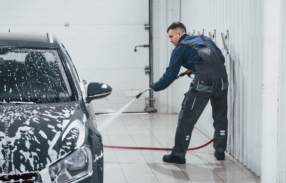 Fototapeta premium Male worker in uniform washing new modern car that covered with soap. Conception of service