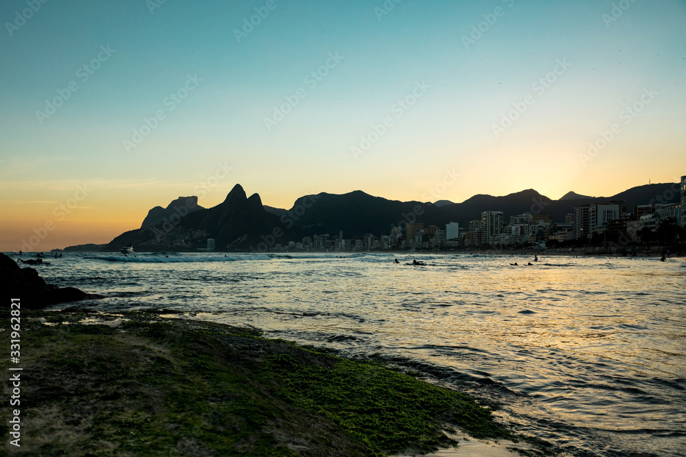Sunset view of Ipanema beach, Leblon beach and Dois Irmão mountain, in Rio de Janeiro, Brazil. Urban landscape with mountain ville on the beach of Ipanema and people surfing in the sea.