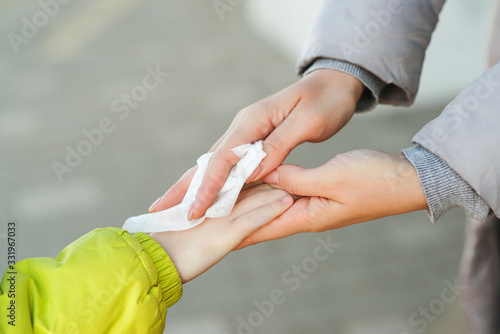 Woman cleaning kid hands with antiseptic tissue outdoors. Hands hygiene. Female using a antibacterial wet napkin wipe.