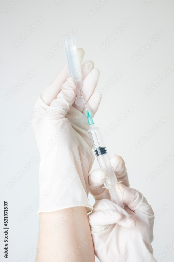 Hands protected with medical gloves, holding a syringe with a needle while preparing to withdraw the substance from the vial as a cure and treatment against viruses and other infectious diseases, COVI Hands protected with medical gloves, holding a syringe with a needle while preparing to withdraw the substance from the vial as a cure and treatment against viruses and other infectious diseases, COVI