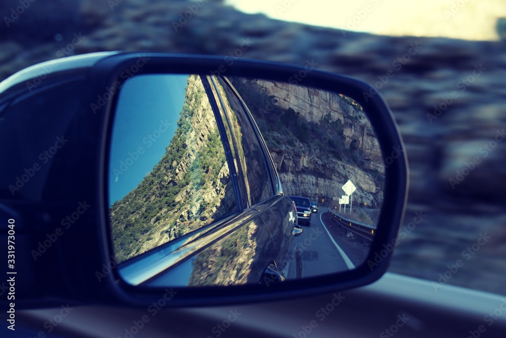 Look in side view mirror with car on the road and reflection of rough desert terrain
