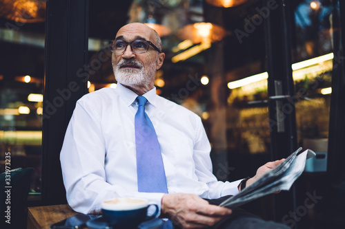 Senior businessman in glasses with newspaper sitting and looking away