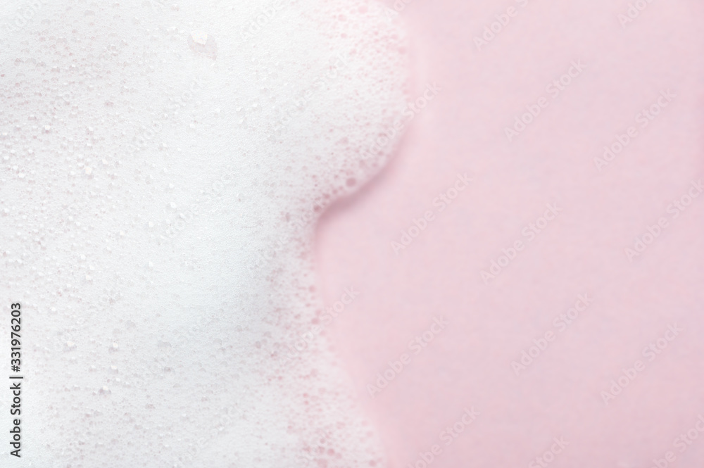 Foaming liquid on pink backdrop. Cosmetics foam background with copy space in right side. Cosmetic product sample of mousse, shampoo or soap. Skincare, cosmetology and beauty concept
