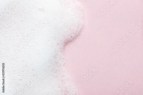 Foaming liquid on pink backdrop. Cosmetics foam background with copy space in right side. Cosmetic product sample of mousse, shampoo or soap. Skincare, cosmetology and beauty concept photo