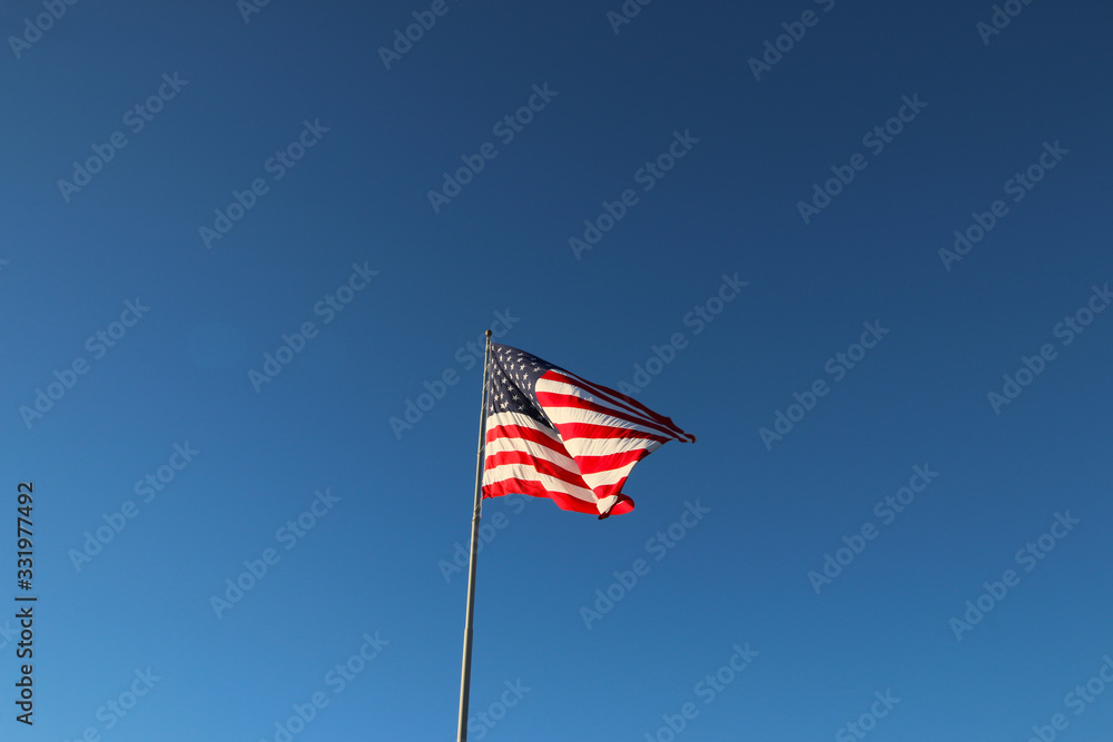 American flag waving in the wind with blue sky background American flag waving in the wind with blue sky background