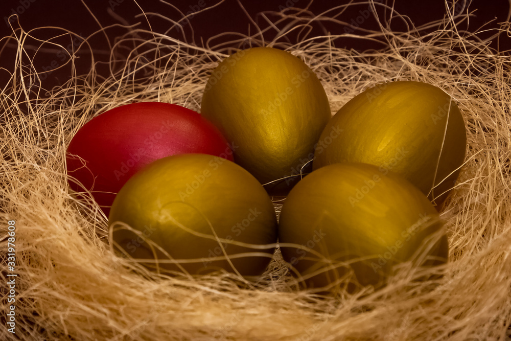 Easter golden eggs and one red egg in the decorative nest on dark brown background. Easter concept. Happy Easter greeting card. Easter golden eggs and one red egg in the decorative nest on dark brown background. Easter concept. Happy Easter greeting card.