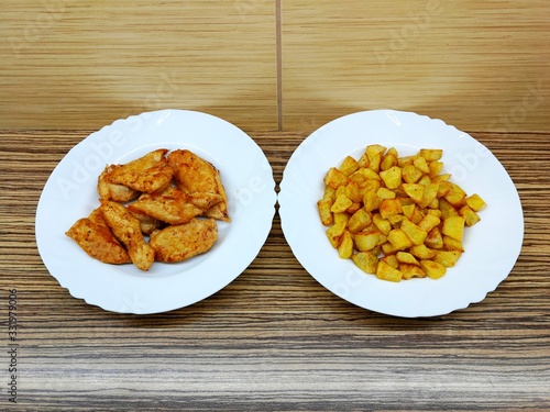 Fried chicken and fried potatoes on two white porcelain plates