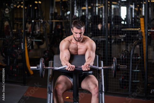 Sexy muscular man sitting on the bench and doind biceps exercise. Front view