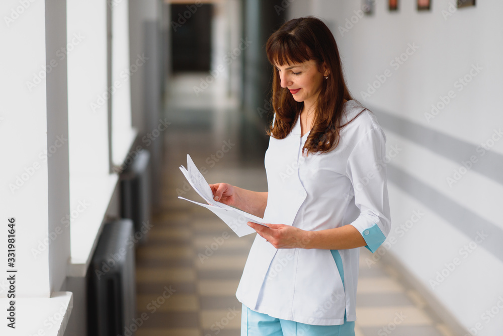 Smiling nurse holding a file while standing in a hallway Smiling nurse holding a file while standing in a hallway