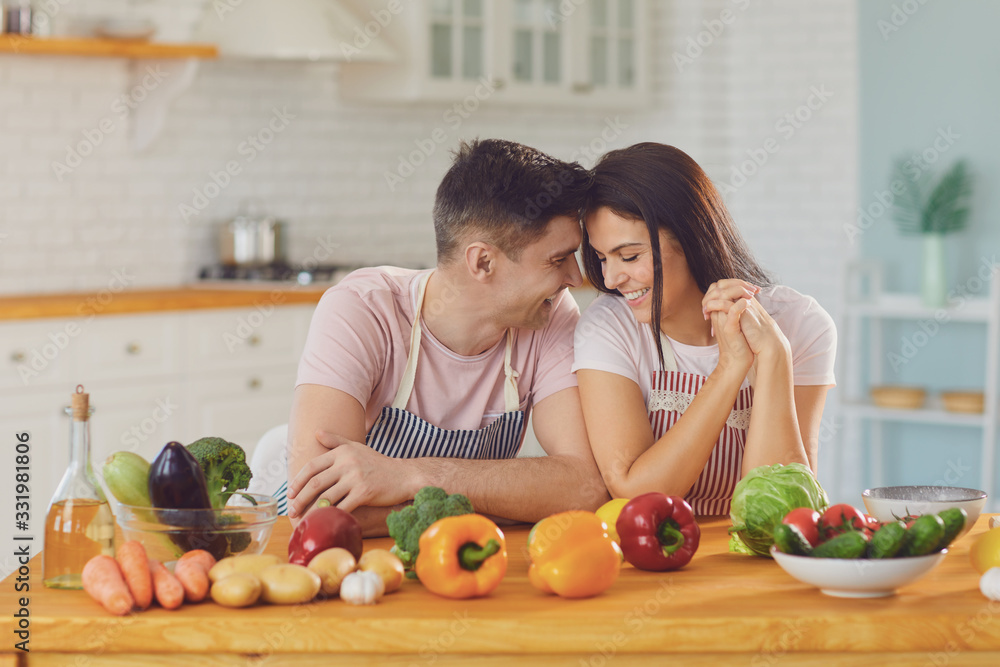 Happy middle couple smiling at a table with fresh vegetables make salad in the kitchen. Happy middle couple smiling at a table with fresh vegetables make salad in the kitchen.