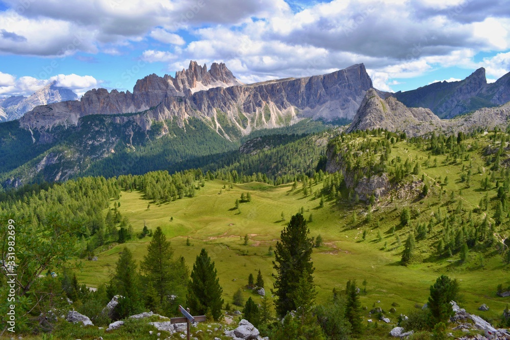 Dolomites mountains, Italy. Sunny day, blue sky, white clouds, green grass. 