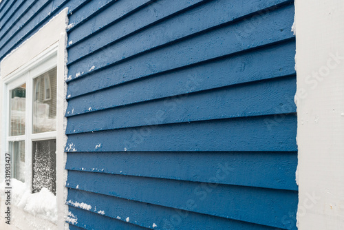 A royal blue wooden clapboard exterior wall of a vintage house. There's a white wooden four pane window and white edge trim on the structure.