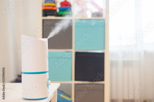 Stylish humidifier on a white table in a children's room. Technologies for humidification and air purification in the area.