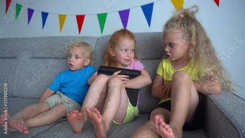 Kids arguing for playing with digital tablet on a sofa. Addictive friends