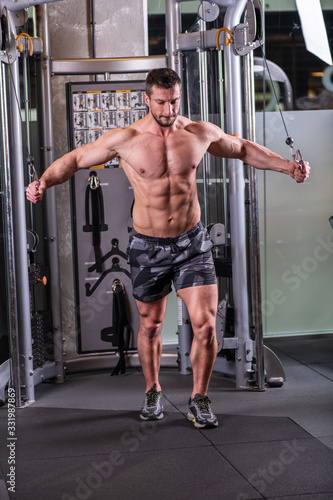 Sexy muscular man doing butterfly exercise for chest on the cable machine