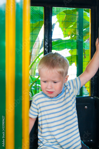 A three-year-old little fair-haired boy rides in a yellow-green children's train in an amusement park in Riviera, Sochi, facing the viewer. © Наталия Пономарева