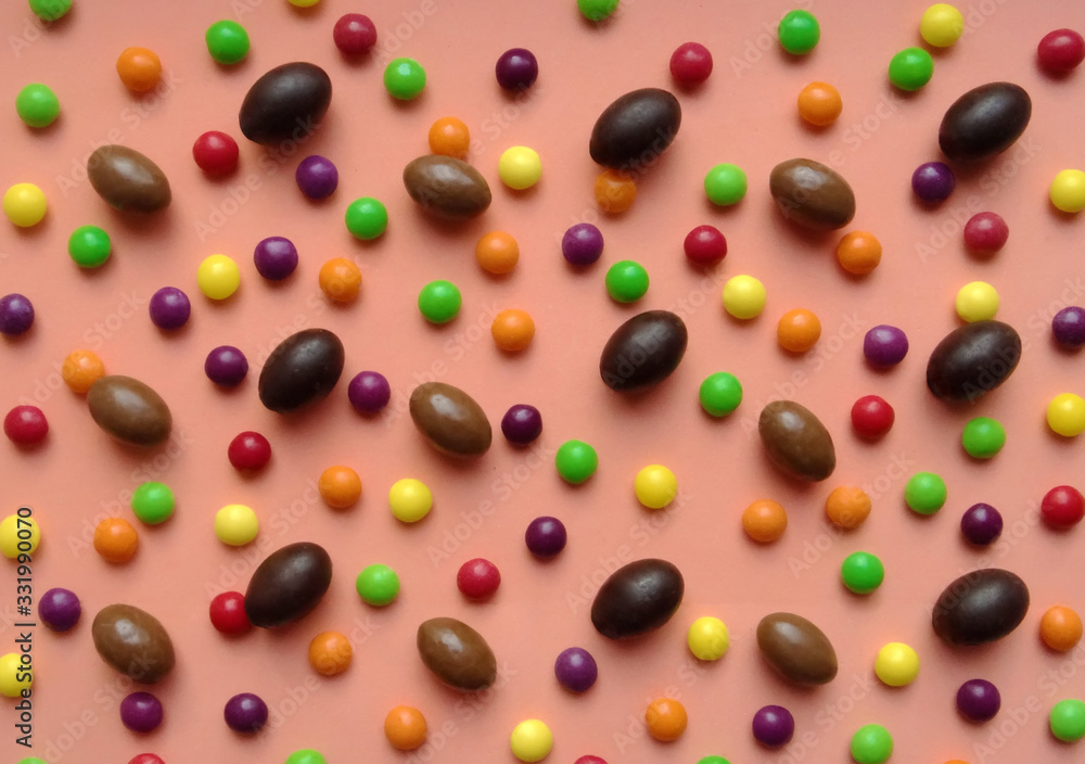 Several chocolate eggs and colorful candies on a peach background in a separate pattern Several chocolate eggs and colorful candies on a peach background in a separate pattern