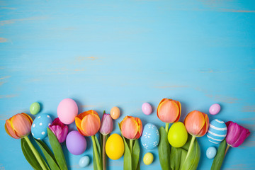Easter holiday background with easter eggs and tulip flowers on wooden table. Top view from above