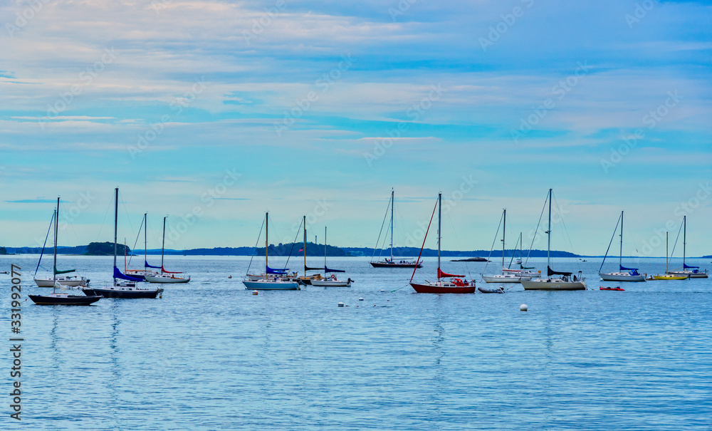 Bouncing up and down on the quiet waves, many sailboats gather in Portland, Maine along the East Promenade harbor