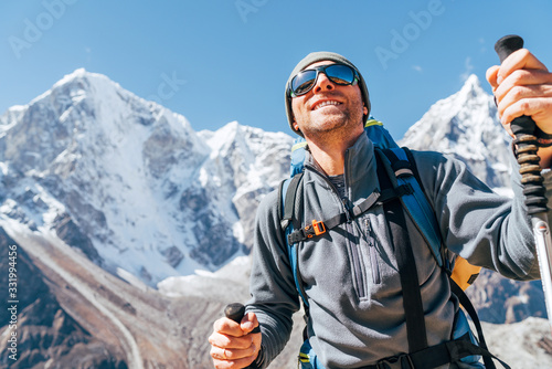 Portrait of smiling Hiker man on Taboche 6495m and Cholatse 6440m peaks background with trekking poles, UV protecting sunglasses. He enjoying mountain views during Everest Base Camp trekking route. photo