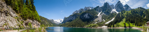 Fototapeta Naklejka Na Ścianę i Meble -  Famous Lake Gosau and Gosaukamm with Mount Dachstein. Spring is here! The snow is melting and spring brings the luscious green back to nature.  The sun is about to hide behind the high peaks.