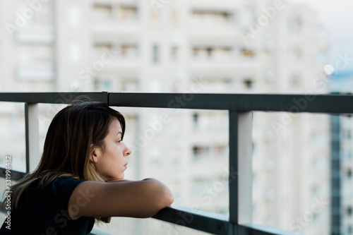 Young sad woman looking outside through balcony of an apartment building