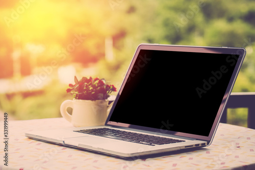 Blank screen computer PC on table with garden view background. Vintage filter.