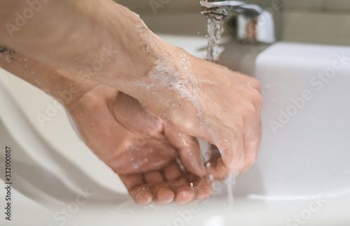 Chico con tatuajes lavándose las manos con jabón debajo de un grifo con agua en un cuarto de baño