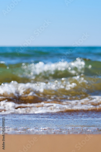 Fototapeta Naklejka Na Ścianę i Meble -  Sandy beach with waves and foam as a natural background with reflection of sunlight on water. Summer holiday concept.