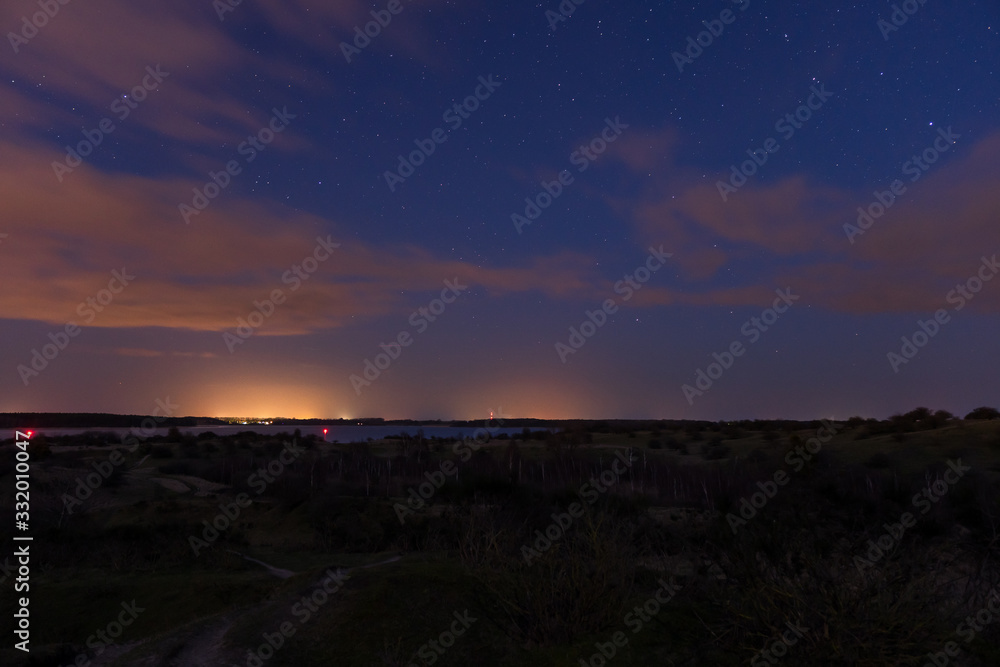 Landscape shot of the night sky with stars and clouds captured on the hilly peninsula Devin near Stralsund and Ruegen with the ocean in the background