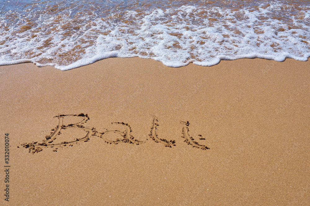 Bali inscription on a tropical sandy beach with waves and foam on a background. Bali inscription on a tropical sandy beach with waves and foam on a background.