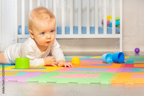 Beautiful baby toddler crawl on the floor of nursery grabbing toys near crib