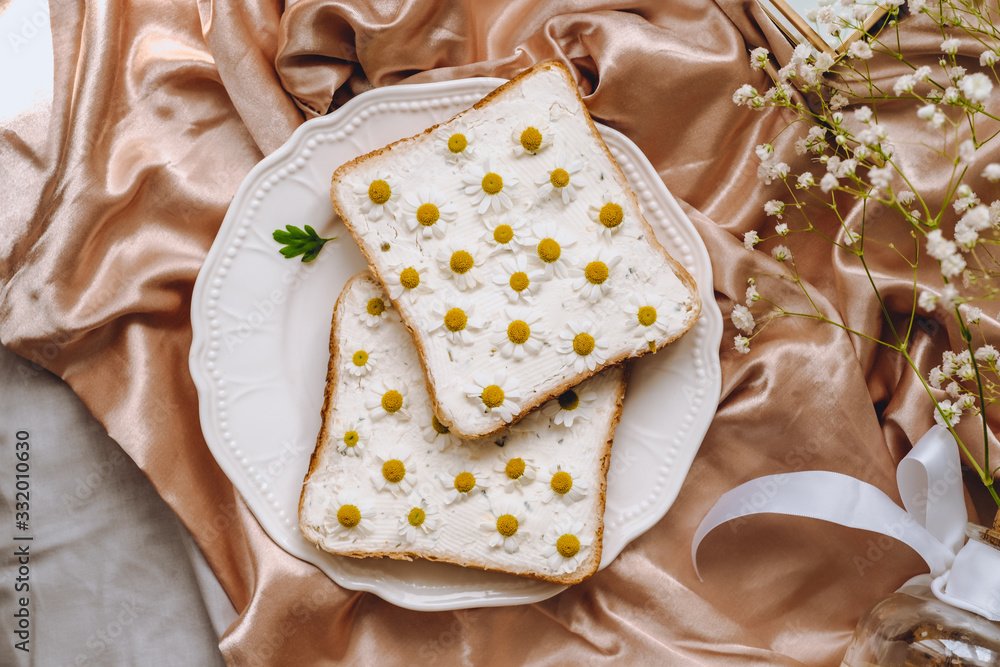 Toast bread sandwich with chamomile flowers in a white plate, on a golden satin fabric with gypsophila flowers Toast bread sandwich with chamomile flowers in a white plate, on a golden satin fabric with gypsophila flowers