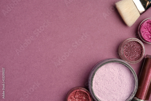 Glitter, lipstick, lip gloss, eye shadow, brush and powder in stand on a plum background from the right edge of the frame
