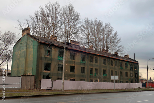 old three-story building, covered with a green grid for repairs on the street behind a gray fence © Sergey