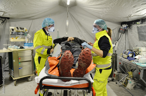 Alert pandemic Covid-19. Doctors with protective masks assist a man with Corona Virus lying on a stretcher inside an Emergency Triage Hospital field tent for the first AID. Global warning alert.  photo