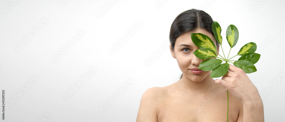 Portrait of pretty dark-haired naked lady hiding half face behind leaf looking at camera, isolated Portrait of pretty dark-haired naked lady hiding half face behind leaf looking at camera, isolated