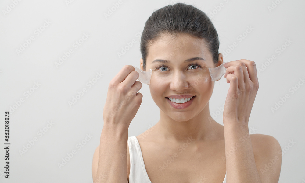Glad young female taking under eye patches off looking at camera, isolated on white background Glad young female taking under eye patches off looking at camera, isolated on white background