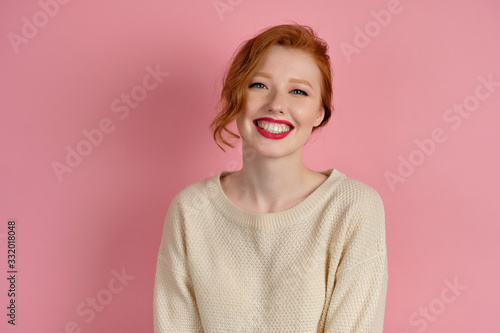 Cute red-haired girl with red lipstick and collected hair smiles beautifully on a pink background photo