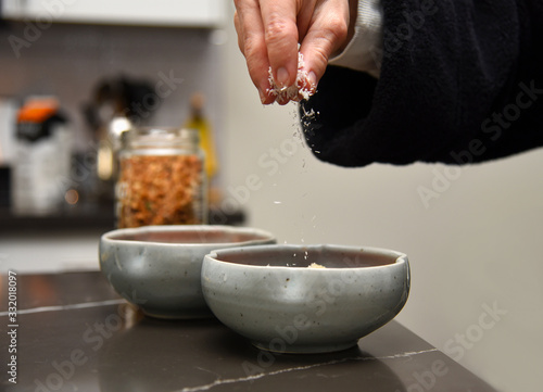 Woman’s hand sprinkling coconut shavings into a ceramic bowl while making a granola smoothie