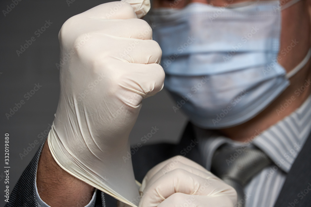 a man with a mask on his face for antivirus individual protection puts on medical sterile gloves - healthcare and medicine concept, prevention tips