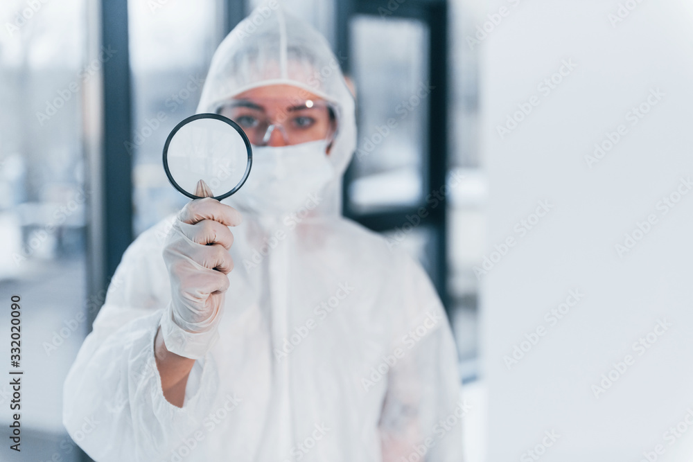 Holds magnifier. Portrait of female doctor scientist in lab coat, defensive eyewear and mask Holds magnifier. Portrait of female doctor scientist in lab coat, defensive eyewear and mask