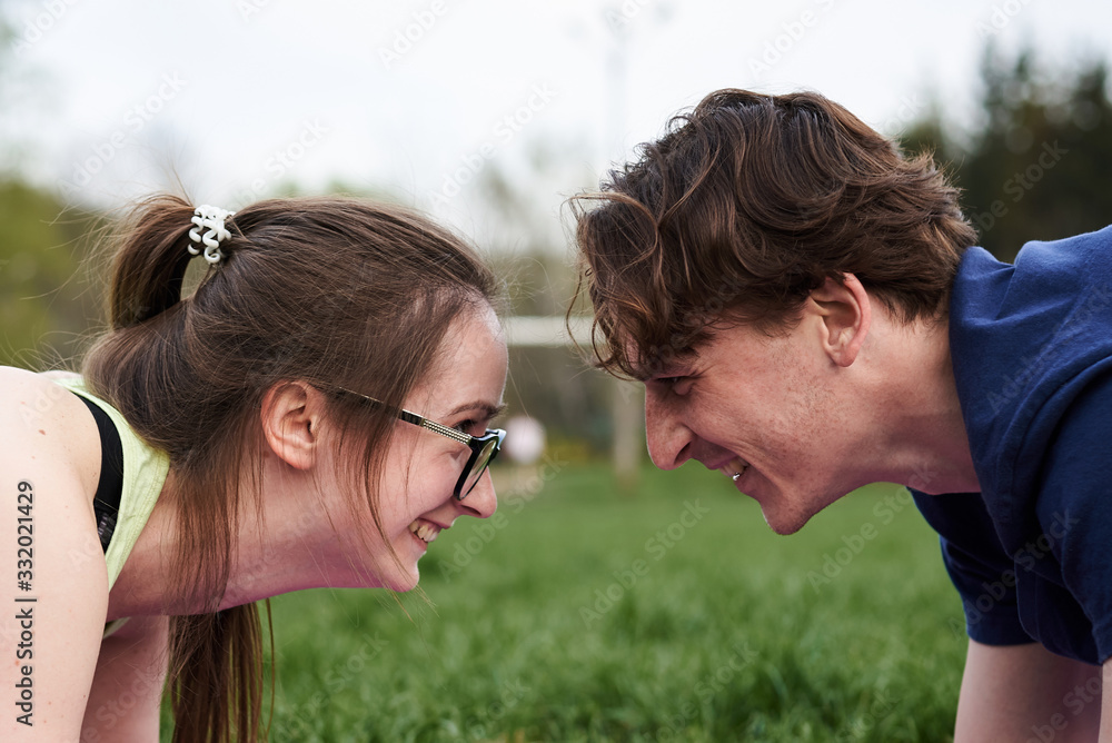 Young couple in love, doing sport exercises together. Close-up picture of brunette woman in eyeglasses together with curly man, looking at each other, smiling, laughing. Romantic relationship.