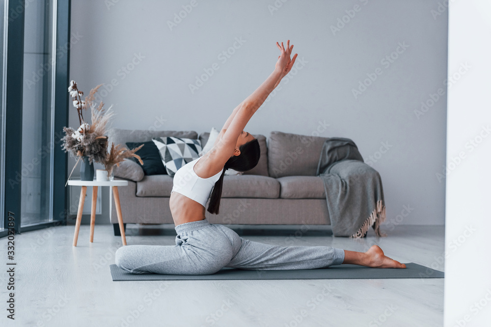 Does flexible exercises. Young woman with slim body shape in sportswear have fitness day indoors at home