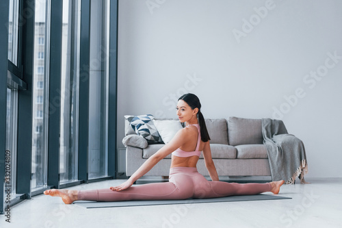 Does exercises on mat on the floor. Young woman with slim body shape in sportswear have fitness day indoors at home