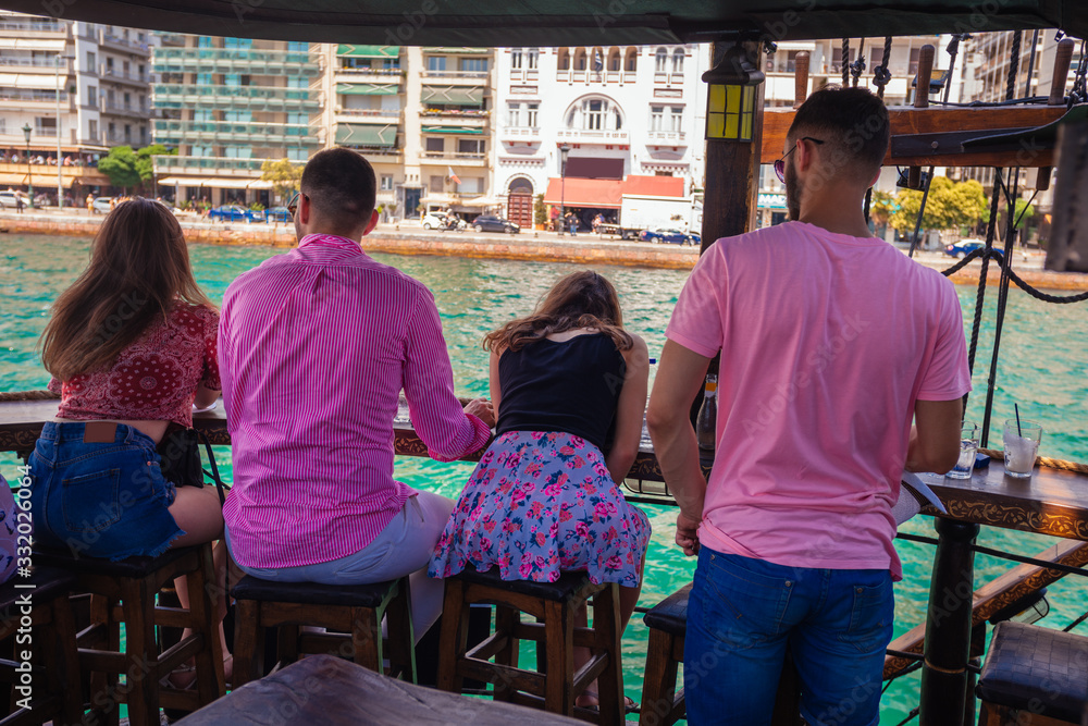 Rear view of four friends sitting in the front of the boat and enjoying the sea looking over the city