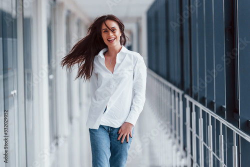 Brunette in white shirt walks indoors in modern airport or hallway at daytime