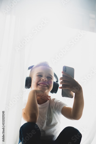 Little smiling boy in casual use smartphone and headphones