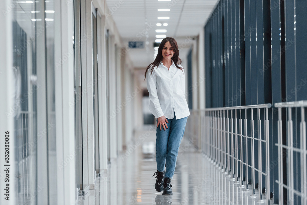 Brunette in white shirt walks indoors in modern airport or hallway at daytime Brunette in white shirt walks indoors in modern airport or hallway at daytime