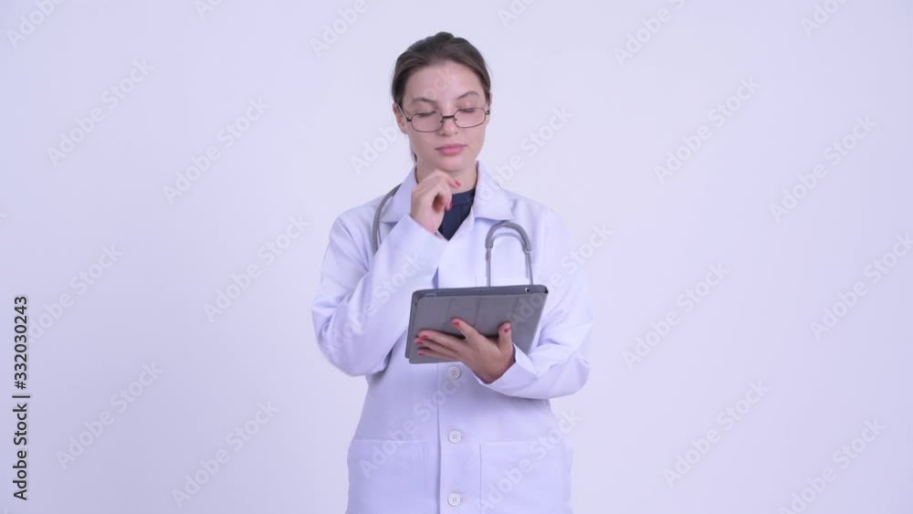 Happy young beautiful woman doctor thinking while using digital tablet Happy young beautiful woman doctor thinking while using digital tablet